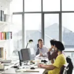 persone in un ufficio grande con grosse vetrate, clienti e impiegati
