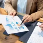 primopiano di una scrivania dove si intravedono due persone, una mostra un grafico ad un'altra