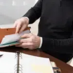 immagine di persona seduta alla scrivania di cui non si vede il volto che sfoglia un faldone di documenti sopra una scrivania